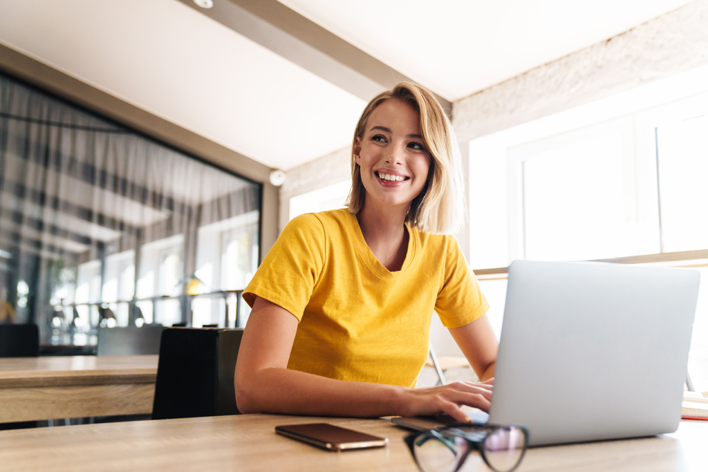 Photo of joyful blonde woman using laptop and smiling