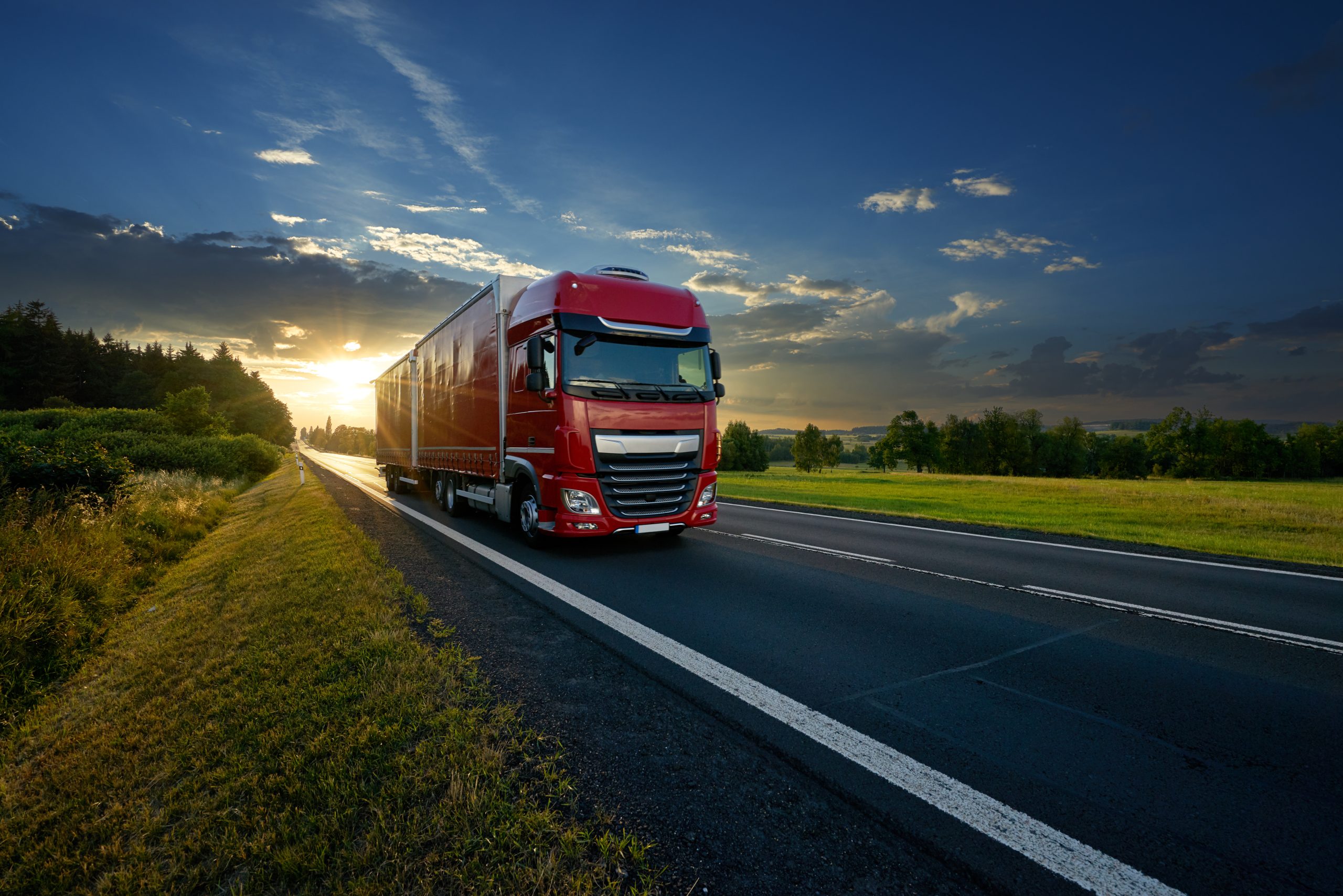 Red truck arriving on the asphalt road in rural landscape in the