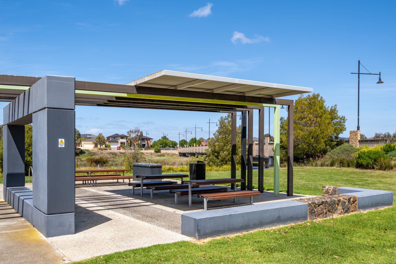 Urban or suburban park amenities in Australia – a modern outdoor public shelter with a sleek design featuring concrete pillars and a roof, complete with built-in seating areas for visitors to rest.