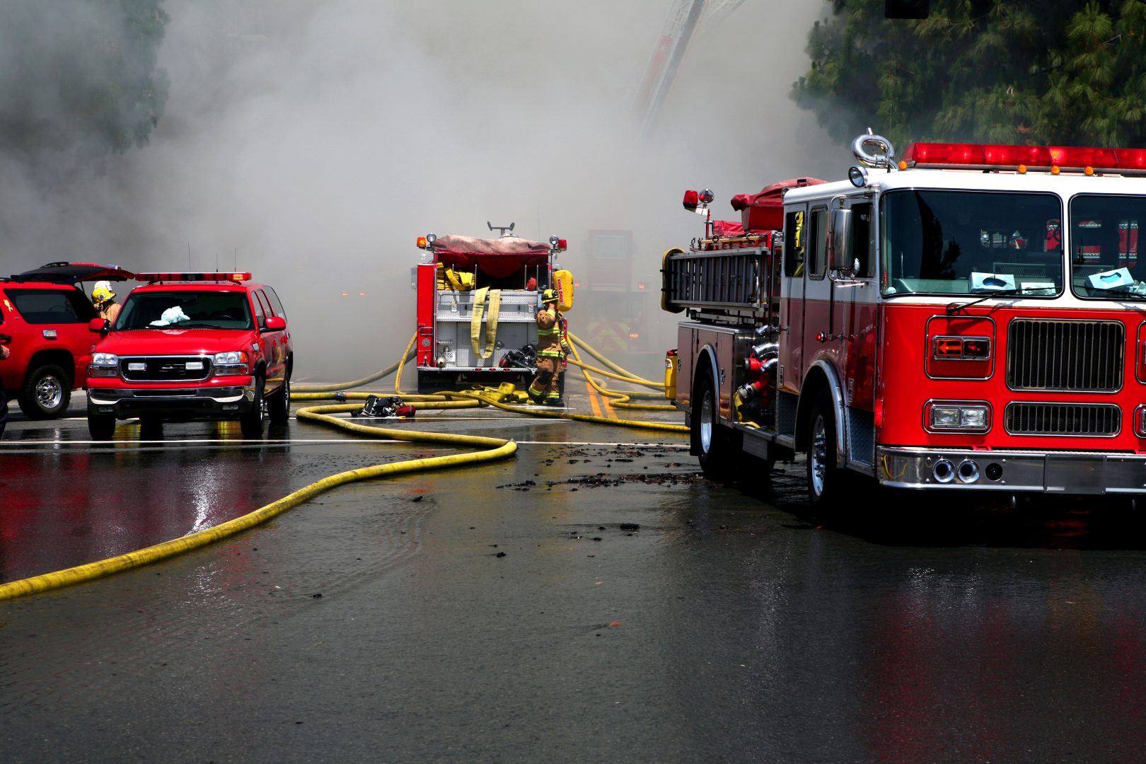 A smoke filled street with yellow fire hoses and fire engines.