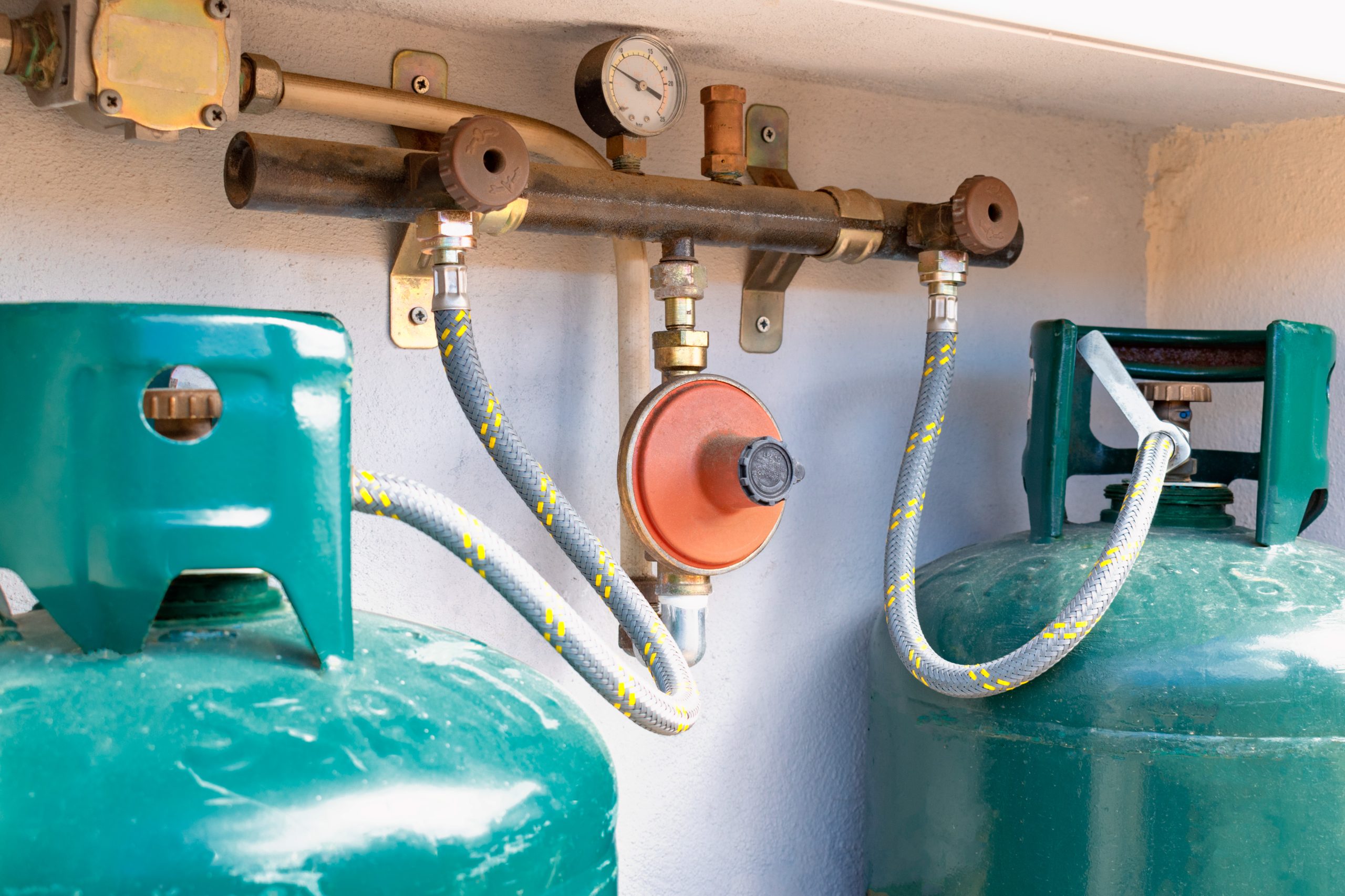 Close up on two gas cylinders connected to the LPG regulator and to the residual gas detector. Double gas cylinders for domestic use with outdoor installation.