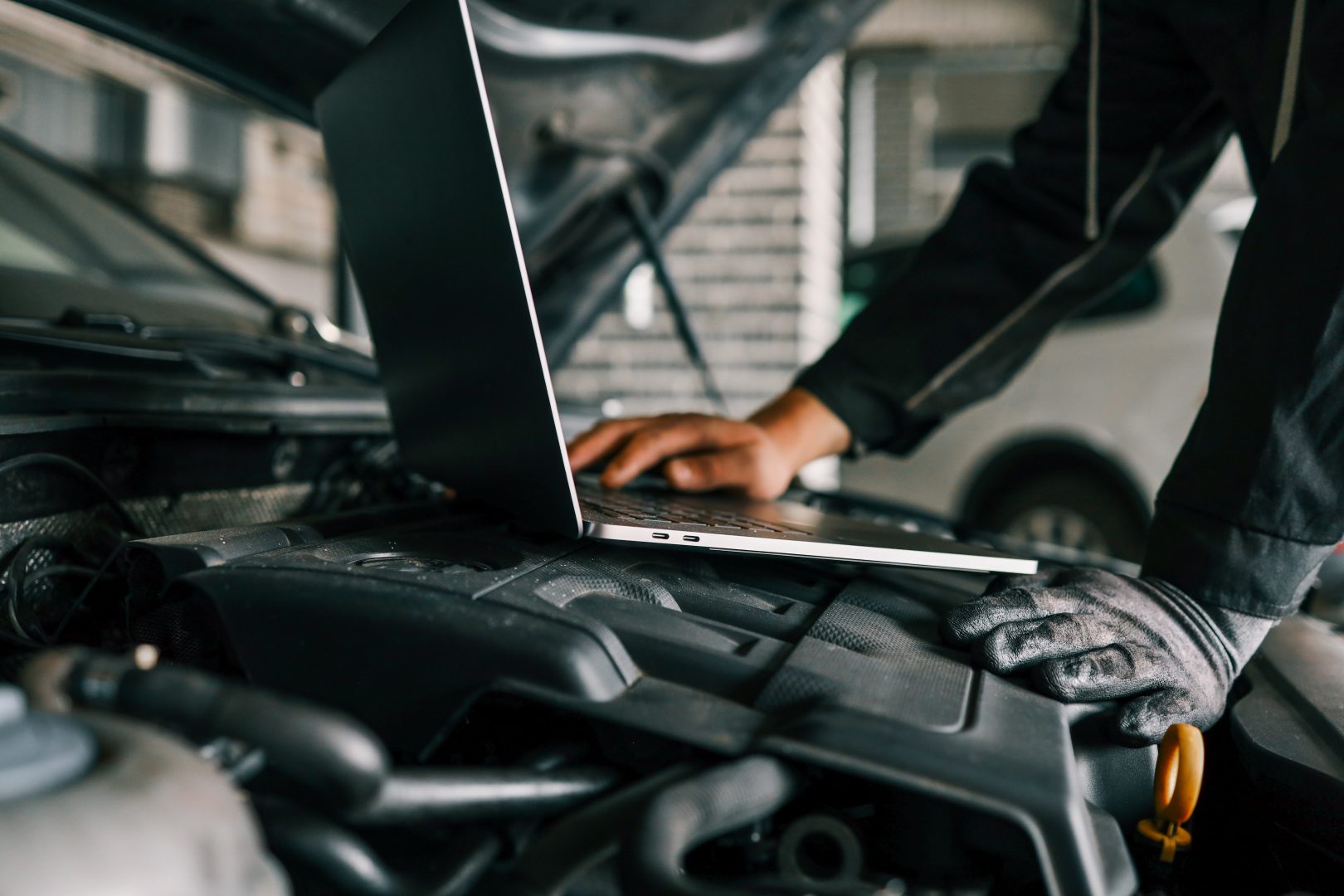 A mechanic using a laptop on a car engine for diagnostics in a garage. Highlights the use of technology in modern vehicle maintenance and repair